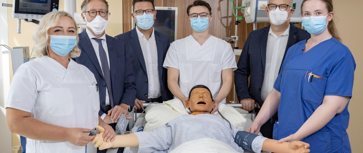 6 Personen stehen um einen Dummy, der eine Pflegepuppe simuliert