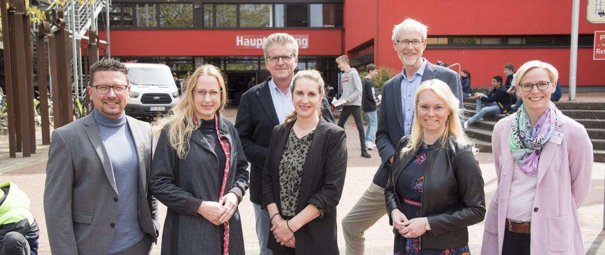 Sieben Personen stehen vor einem Schulgebäude.