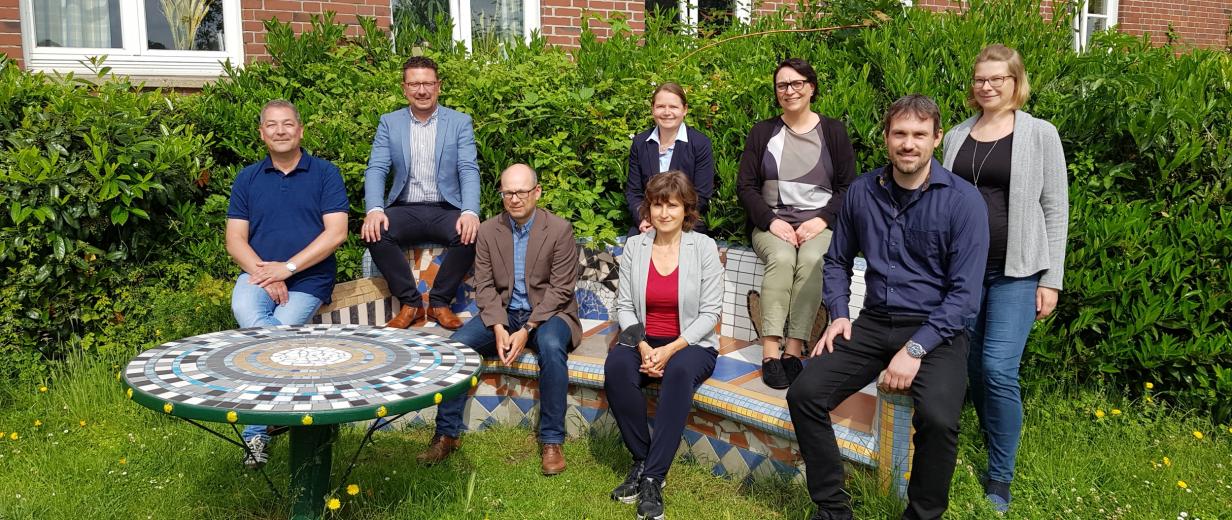 Eine Personengruppe sitzt auf und steht an einer bunt gefliesten Steinbank