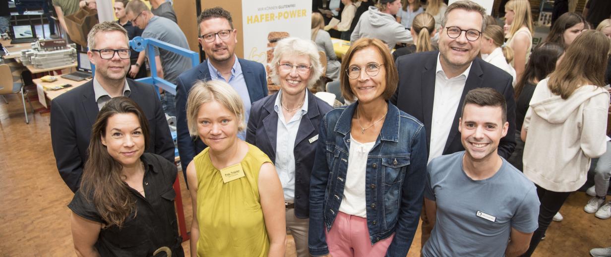 Eine Personengruppe steht im Halbkreis in einem Foyer und schaut in die Kamera.