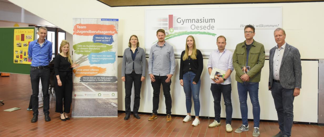 8 Personen vor einem großen Plakat