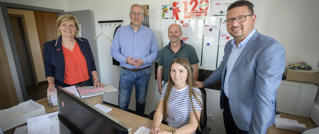 Fünf Personen stehen oder sitzen in einem Büro.