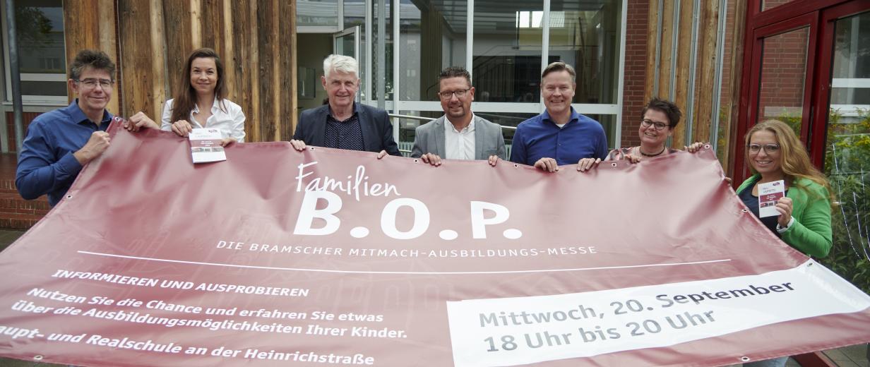 Sieben Personen mit einem Werbebanner in den Händen stehen vor einem Gebäude.