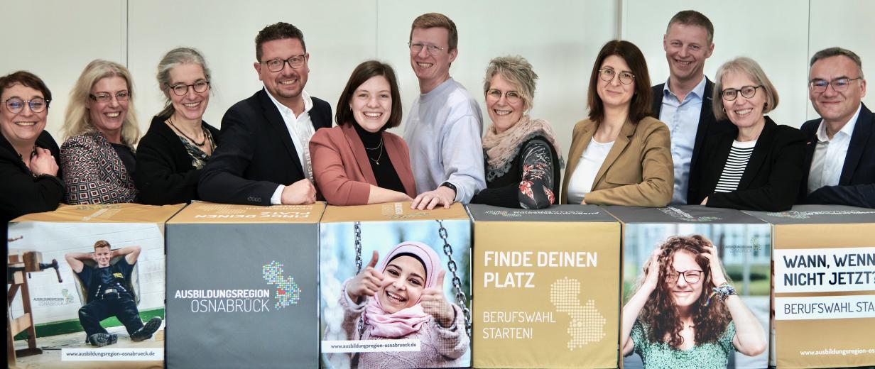 1.000 Chancen für junge Menschen auf einen Ausbildungsplatz in unserer Region Gruppe von Personen vor langem Tresen mit Plakaten