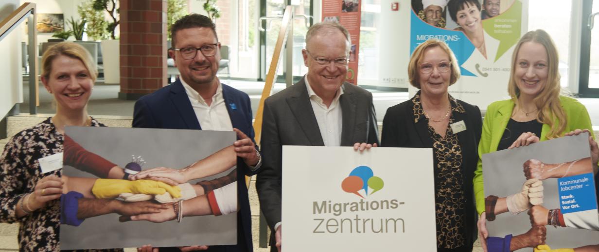 Fünf Personen stehen im Foyer eines Gebäudes vor einer Treppe.