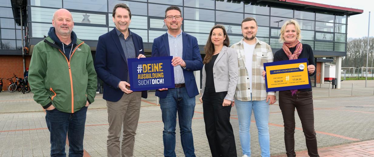 Sechs Personen stehen vor einer Halle mit Glasfassade.