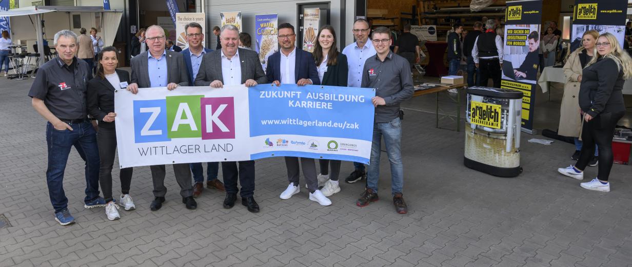 Eine Personengruppe mit einem Banner in den Händen steht vor einer Lagerhalle.