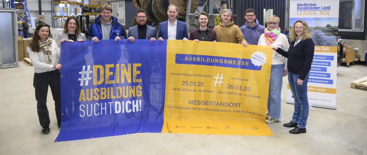 Eine Personengruppe mit einem großen Werbebanner steht in einer Werkshalle.