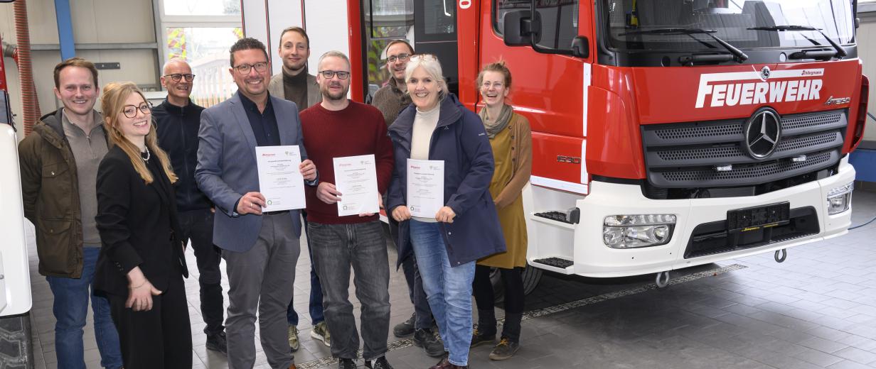 Eine Personengruppe steht neben einem Feuerwehrauto in einer Werkhalle.