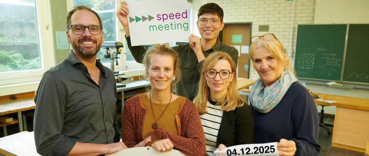 Fünf Personen stehen in einem Klassenraum.