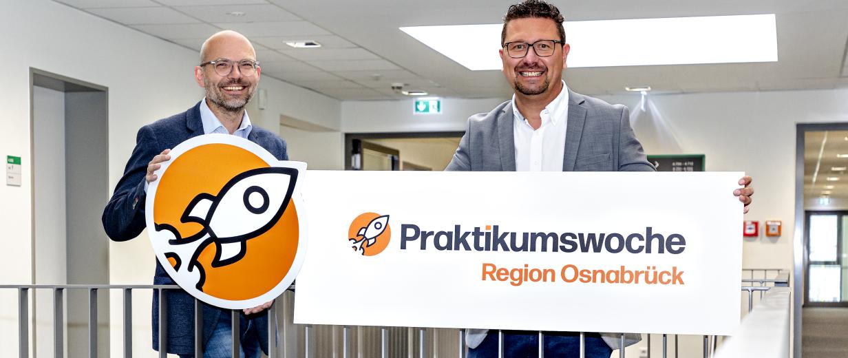 Zwei Personen mit einem Pappschild stehen in einem Treppenhaus.