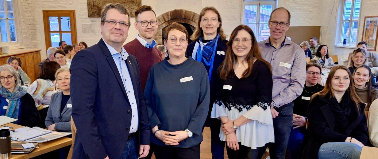 Sechs Personen in einem Vortragsraum zwischen Stuhlreihen