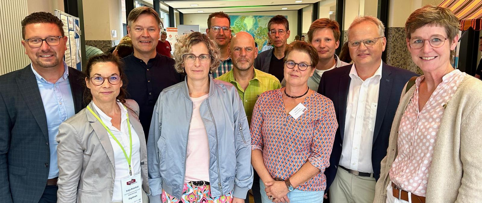 Eine Personengruppe steht im Halbkreis und schaut in die Kamera.