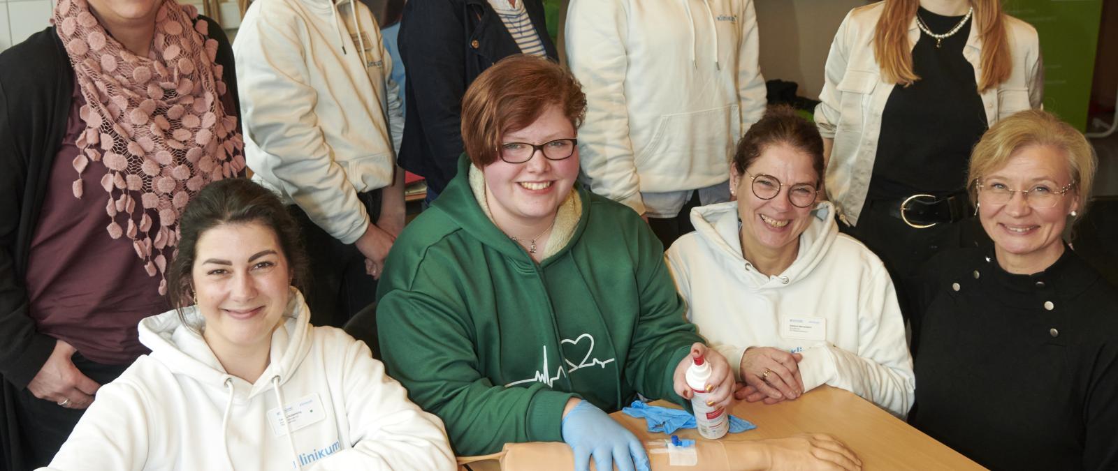 Eine Personengruppe steht und sitzt in einem Klassenzimmer.