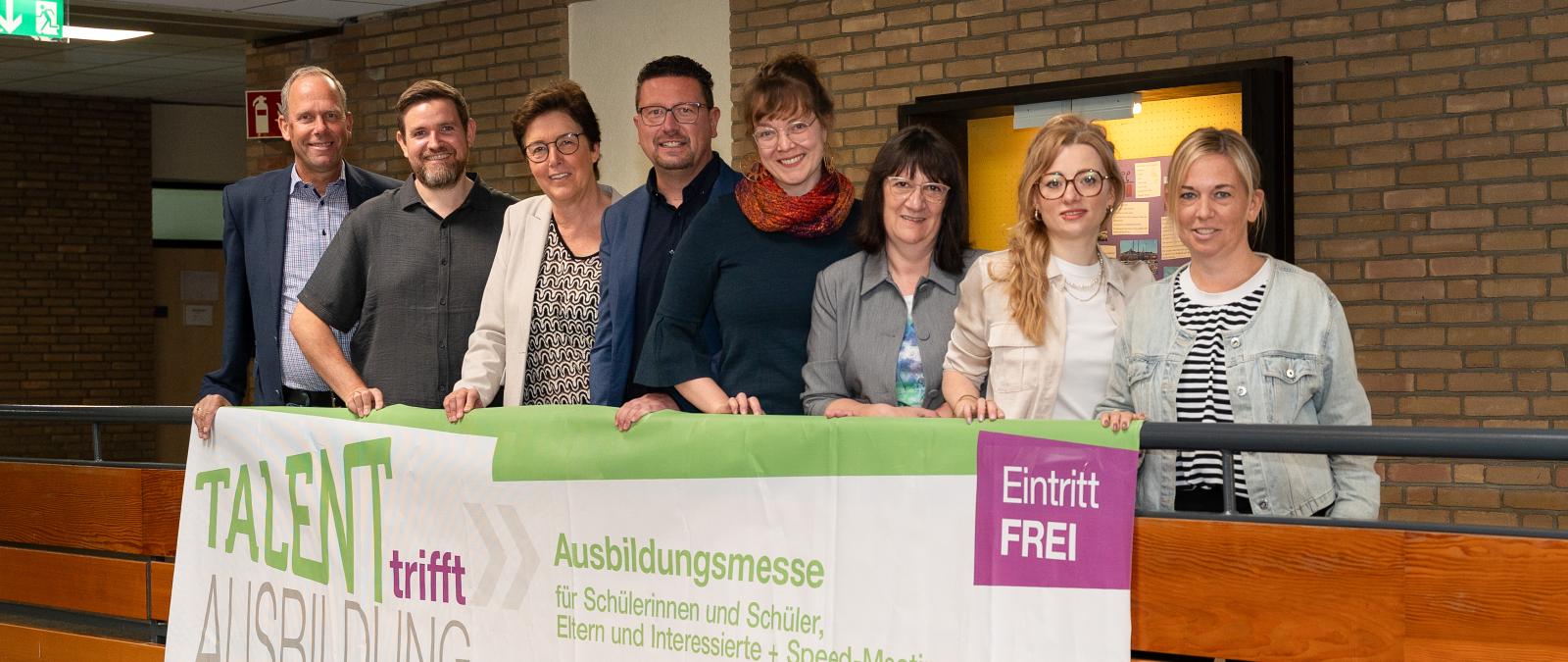 Personengruppe steht auf einer Empore, an der ein Plakat befestigt ist.