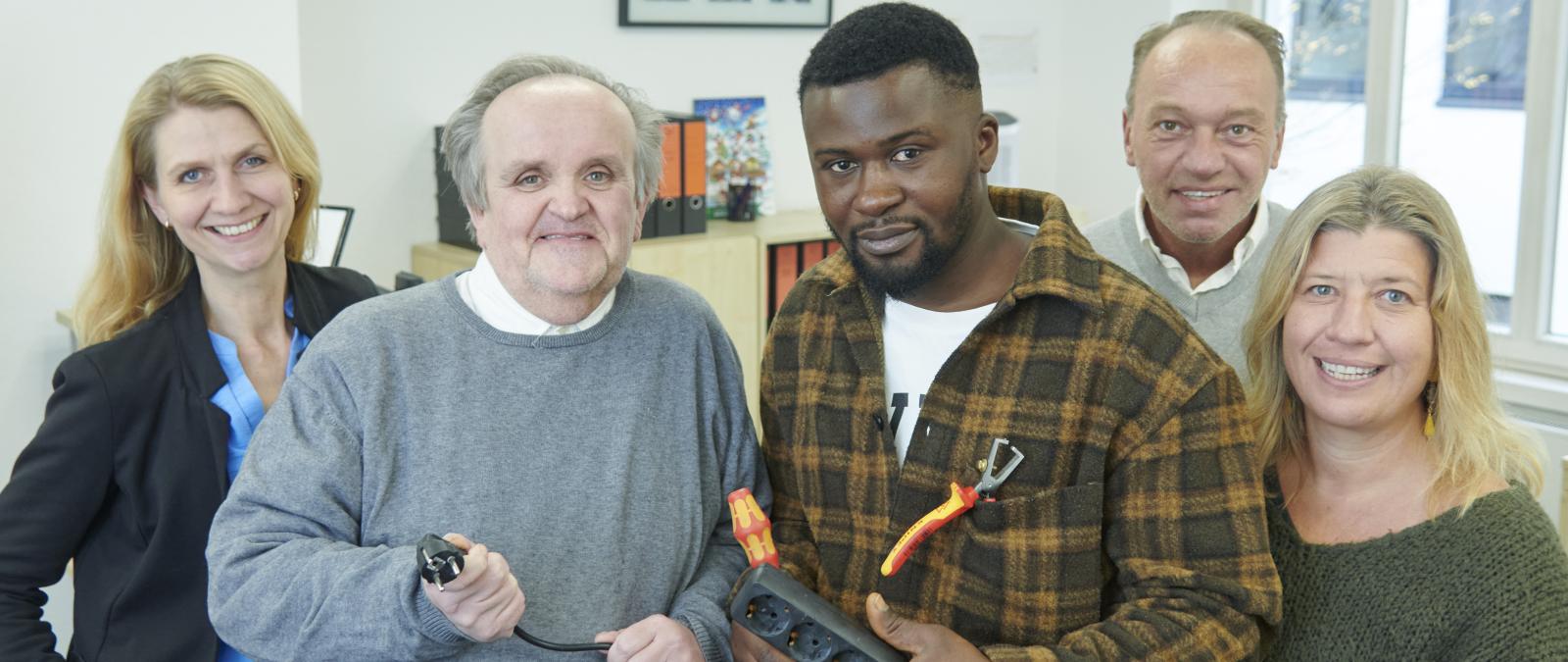 Fünf Personen mit Steckerleiste in der Hand stehen in einem Büro.