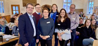 Sechs Personen in einem Vortragsraum zwischen Stuhlreihen