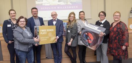 Eine Personengruppe mit bedruckten Schaumstoffwürfeln in den Händen steht vor einer Video-Projektionsfläche.