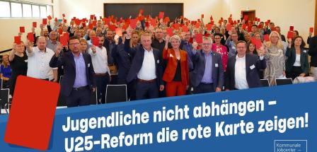 Eine Personengruppe in einem Saal hält rote Karten in die Höhe.