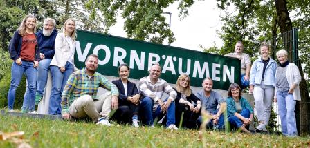 Betriebsbesichtigung Vornbäumen Eine Personengruppe steht, hockt und sitzt vor einem Zaun.