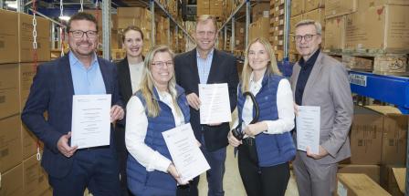 Sechs Personen stehen in einem Hochregallager.