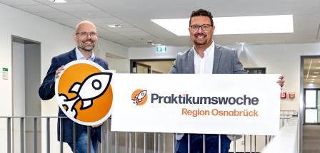 Zwei Personen mit einem Pappschild stehen in einem Treppenhaus.