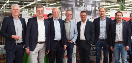 Sieben Personen stehen in einer Werkhalle.