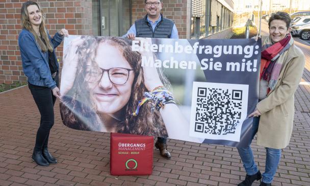 3 Personen halten ein Plakat