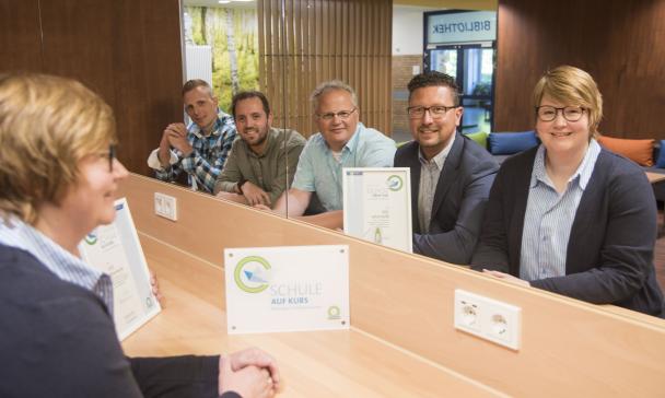 Fünf Personen sitzen vor einer Wand mit einem großen Spiegel.