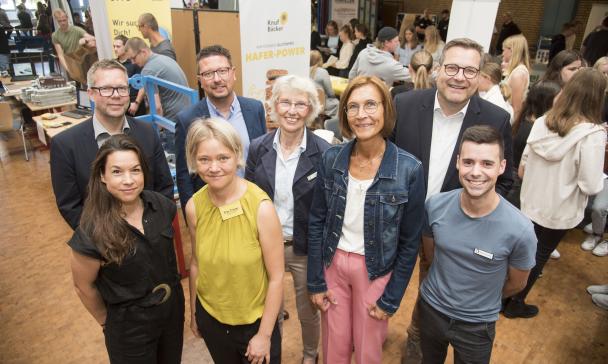 Eine Personengruppe steht im Halbkreis in einem Foyer und schaut in die Kamera.