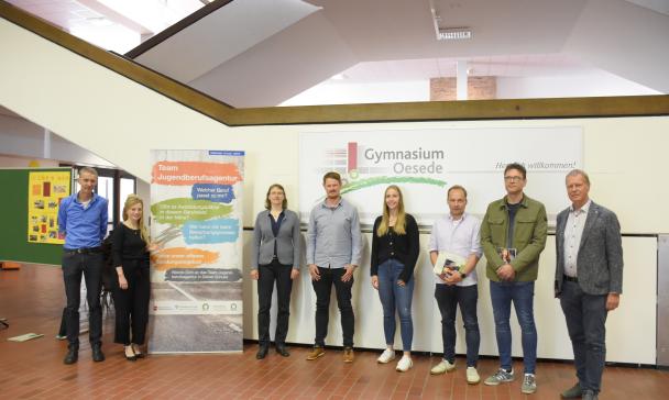 8 Personen vor einem großen Plakat