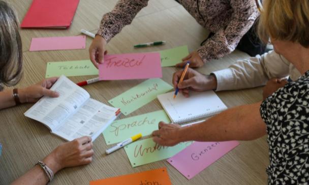 Drei Personen sitzen und stehen um einen Tisch herum.