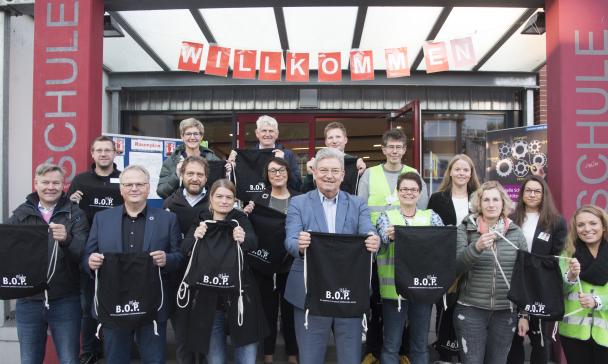 Eine Personengruppe hält Stoffbeutel in die Kamera.