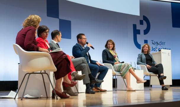 Sechs Personen sitzen auf einer Bühne.