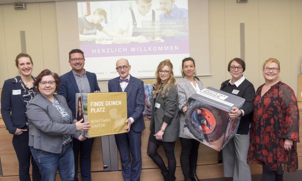 Eine Personengruppe mit bedruckten Schaumstoffwürfeln in den Händen steht vor einer Video-Projektionsfläche.