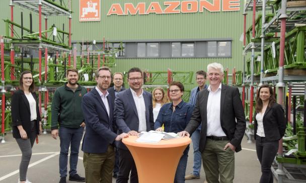 Eine Personengruppe steht vor einem Fabrikgebäude.