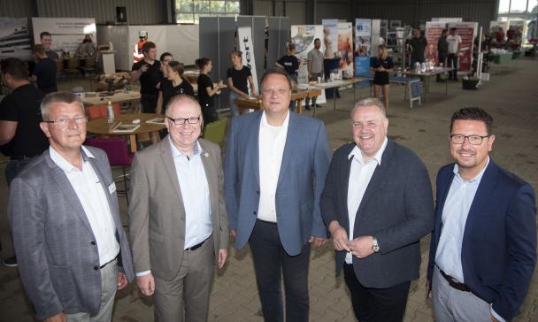 Fünf Personen, die Hemden und Jacketts tragen, stehen in einer Werkhalle.