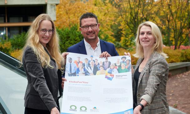 Drei Personen präsentieren ein Plakat.