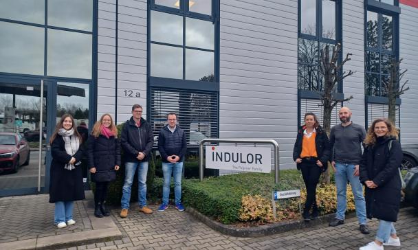 Eine Personengruppe steht vor dem Eingang zu einem Firmengebäude.