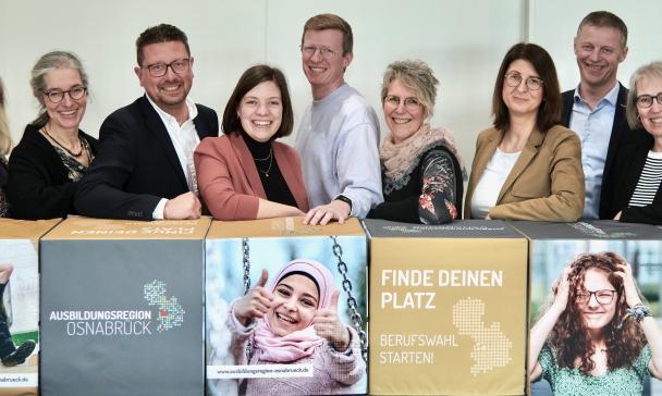 Gruppe von Personen vor langem Tresen mit Plakaten