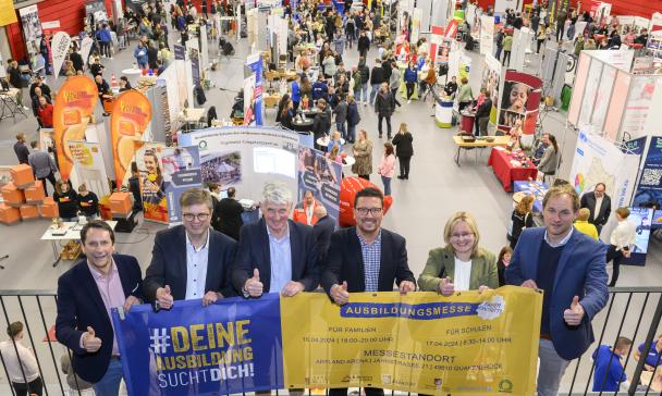 Sechs Personen mit einem Werbebanner in den Händen stehen auf der Empore einer Sporthalle.