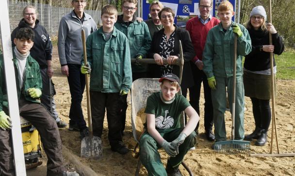 Eine Personengruppe mit Gartengeräten steht auf einer Freifläche.