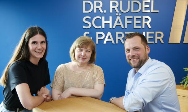 Drei Personen stehen an einem Tisch.