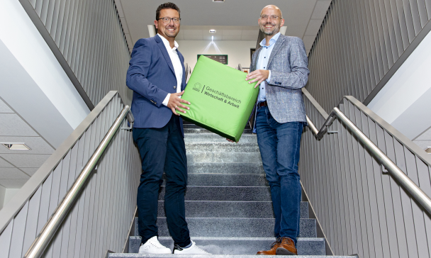 Zwei Personen mit einem großen Würfel in den Händen stehen in einem Treppenhaus.