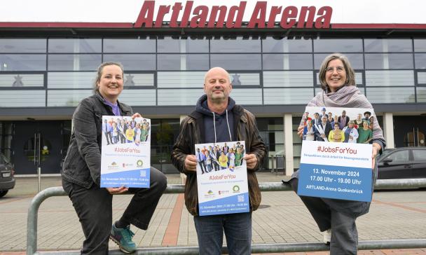 Drei Personen stehen vor einem Gebäude mit Glasfassade.