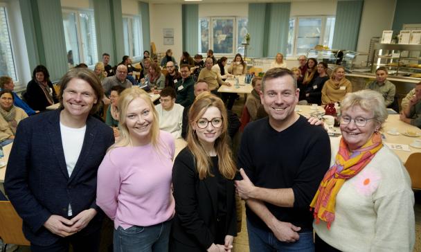 Fünf Personen stehen in einer Reihe im Hintergrund ein Sitzungssaal.
