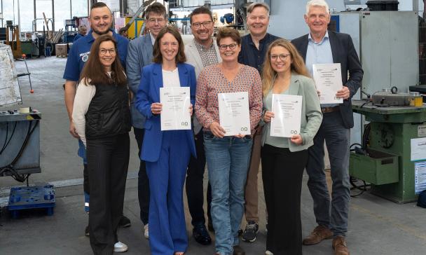 Neun Personen stehen in einer Werkhalle.