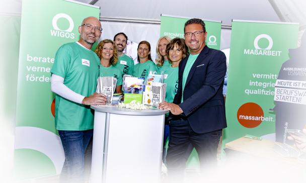 Personengruppe steht an einem Messestand mit Rollups im Hintergrund.