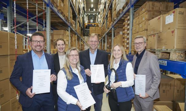 Sechs Personen stehen in einem Hochregallager.