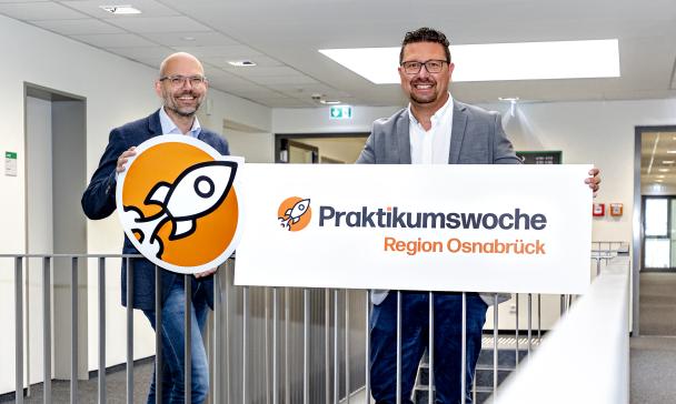 Zwei Personen mit einem Pappschild stehen in einem Treppenhaus.